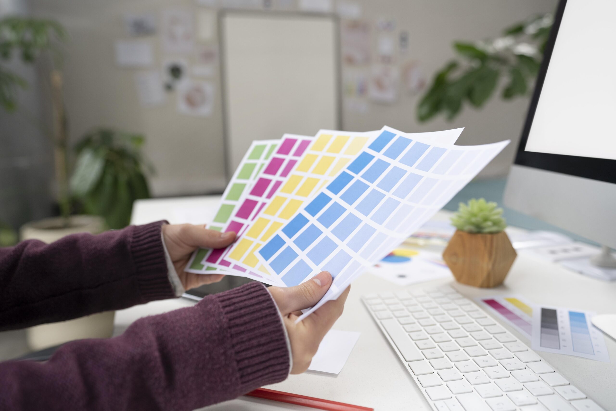 Bir kişi, masa başında farklı renk kartelalarını elinde tutarak baskı ve tasarım için renk seçimi yapıyor.